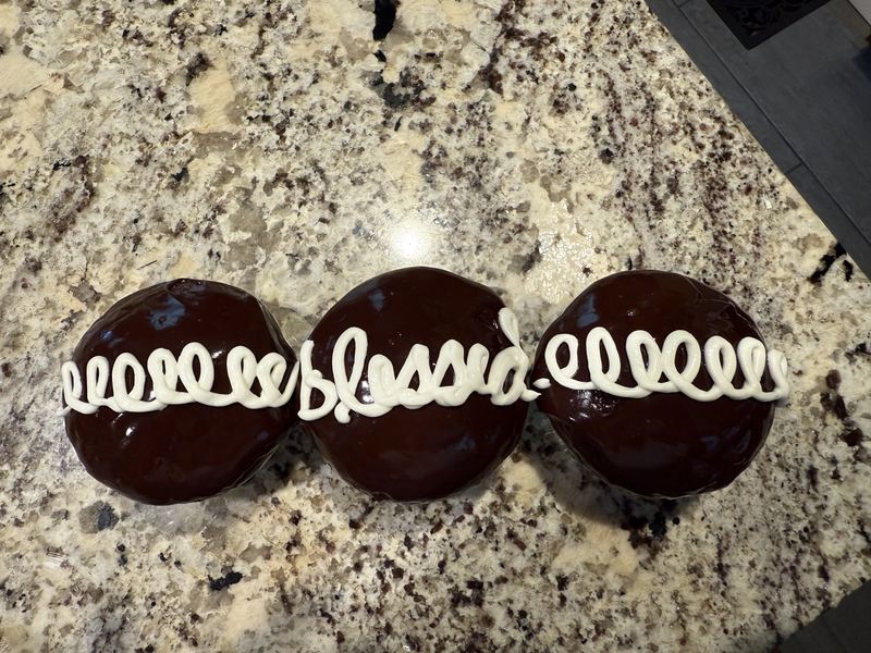 Three chocolate-glazed cupcakes with white icing loops spelling the word blessed