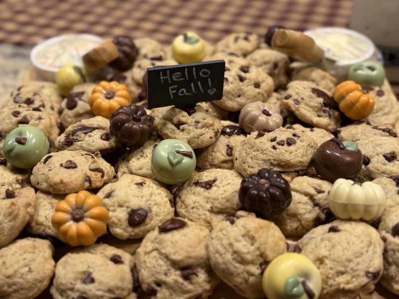 A platter of chocolate chip cookies with chocolate pumpkins and apples and a Hello Fall sign