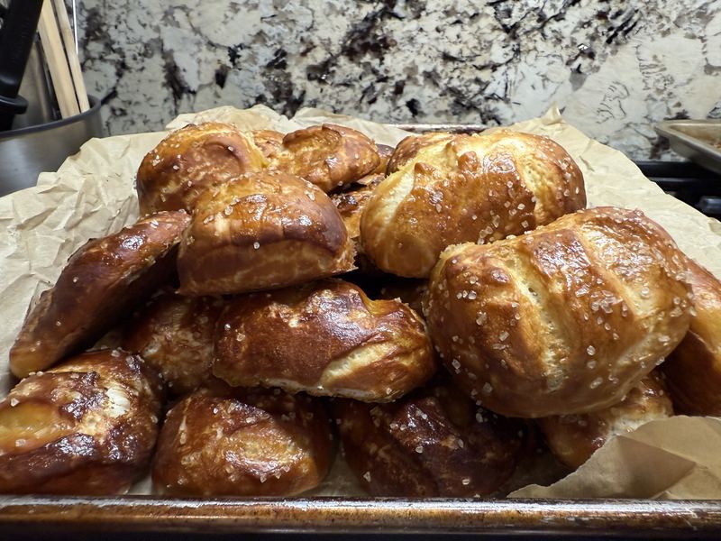 A pile of shiny brown soft pretzel rolls sprinkled with coarse salt