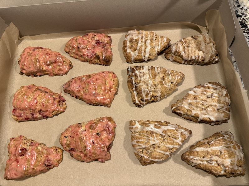A bakery box of pink raspberry-glazed scones and cinnamon scones with icing drizzle